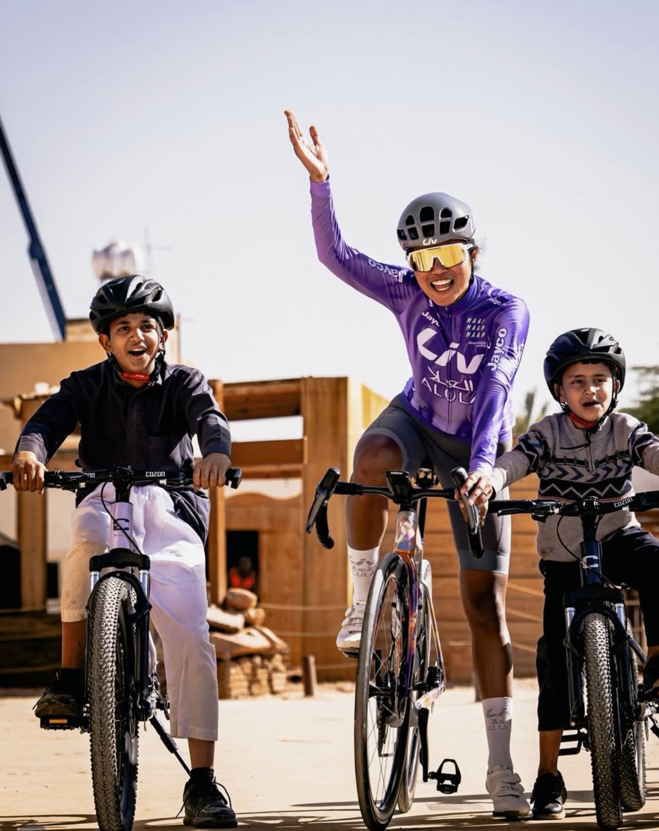 Cycliste en maillot Liv entourée de deux enfants dans le désert d'AlUla