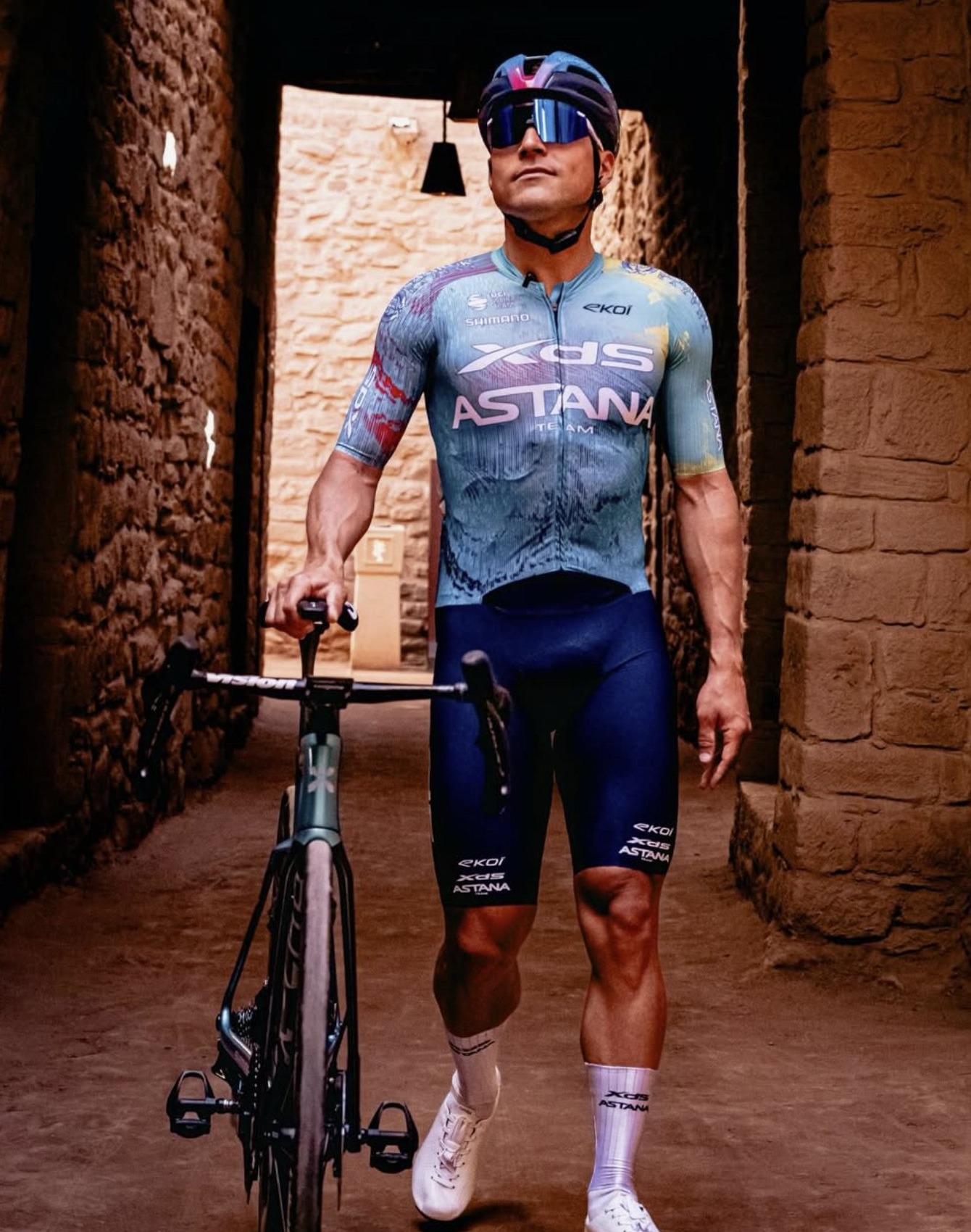 Cycliste Astana marchant avec son vélo dans une ruelle en pierre d'AlUla